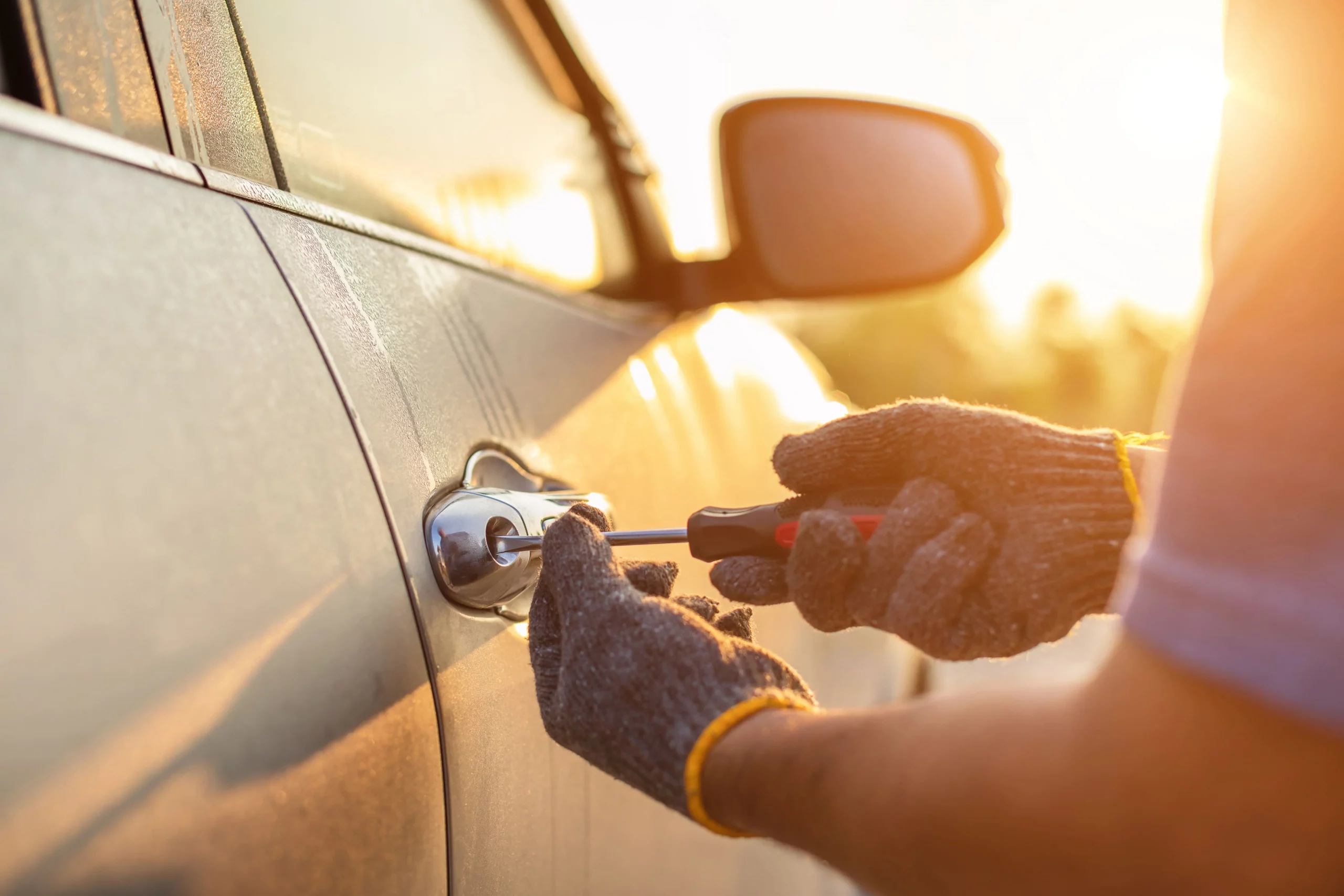 A car technician's hands in gloves using a screwdriver on a car door lock at sunset, symbolizing repair and maintenance.